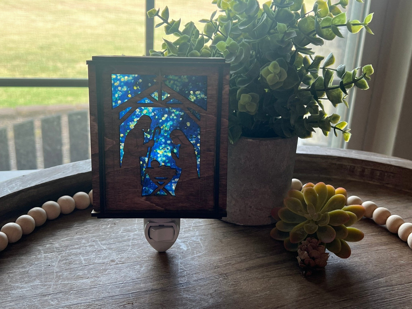 A Christmas Nativity Lantern Nightlight in golden oak with wood and acrylic materials with natural light shining through.