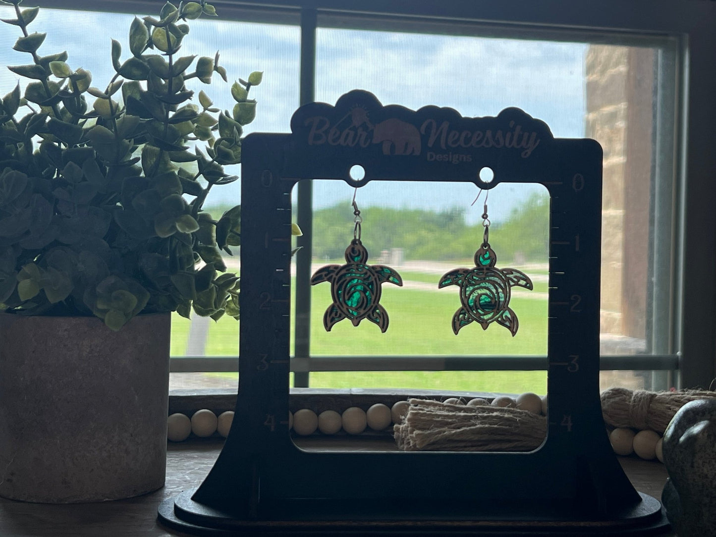 Handmade green and black turtle earrings with stained glass effect, crafted from wood and acrylic in sunlight.