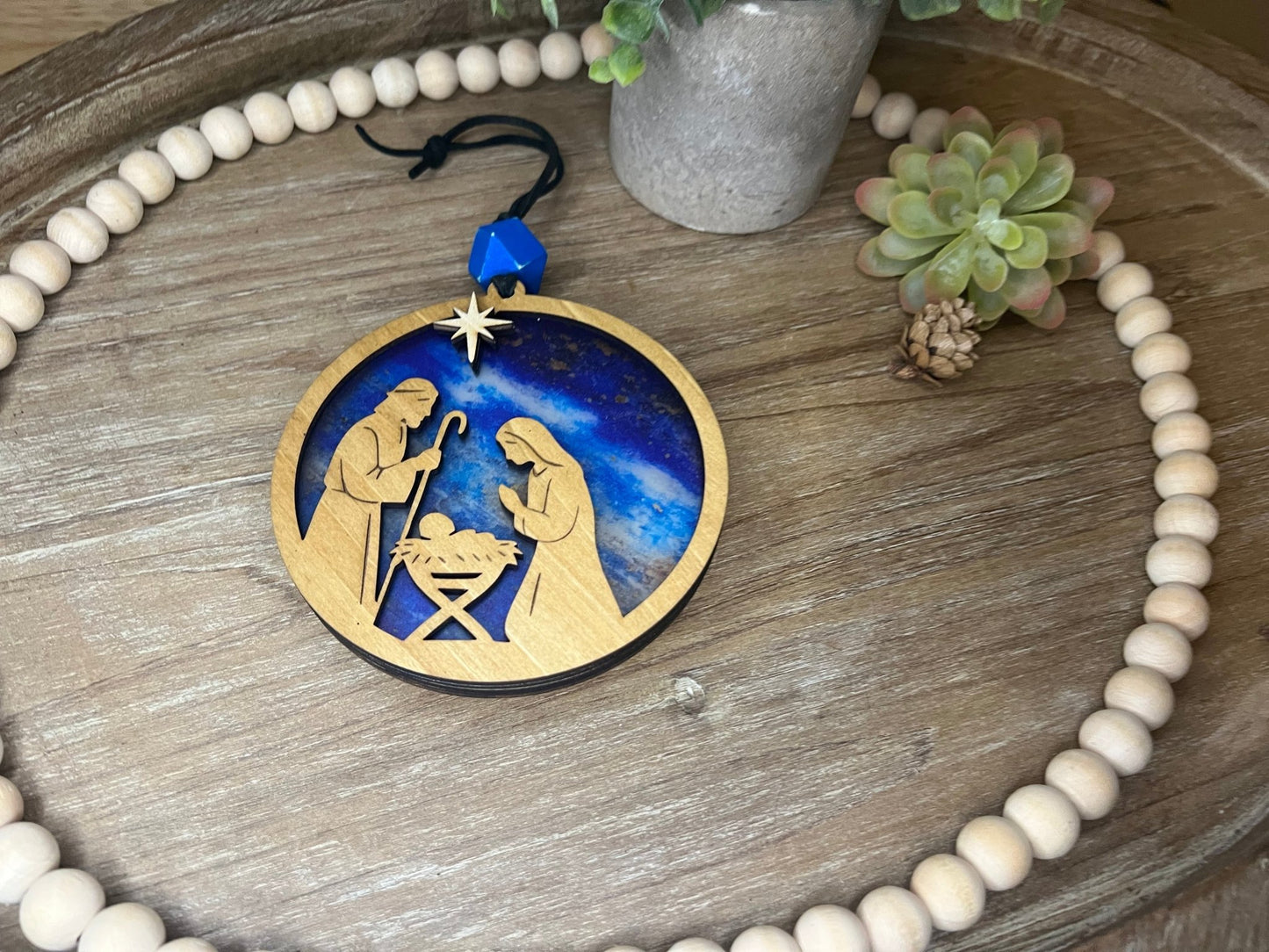 Lighted Christmas Nativity Ornament made of wood and acrylic, featuring a rustic, multicolor design unlit layng on a tray.