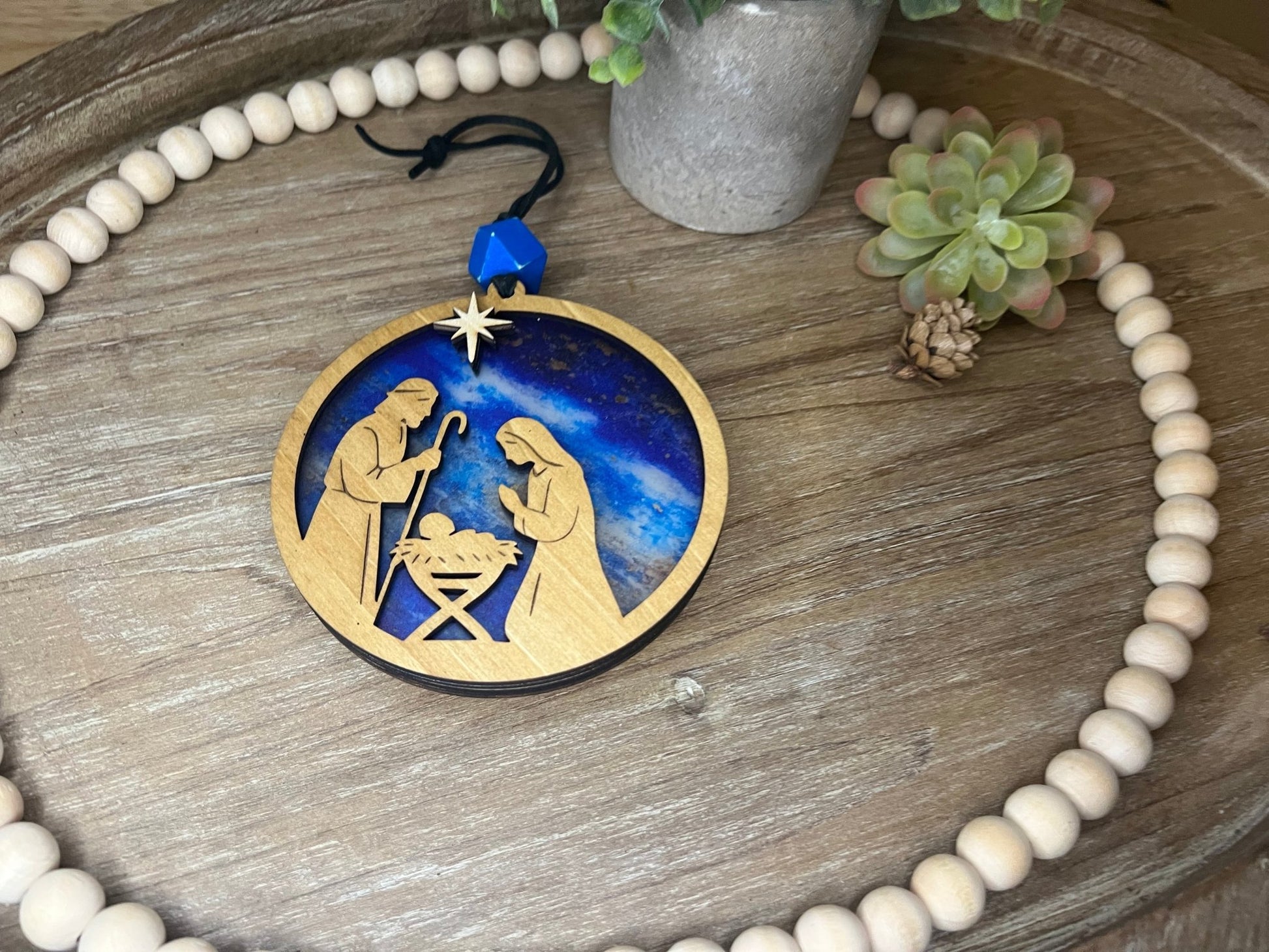 Lighted Christmas Nativity Ornament made of wood and acrylic, featuring a rustic, multicolor design unlit layng on a tray.